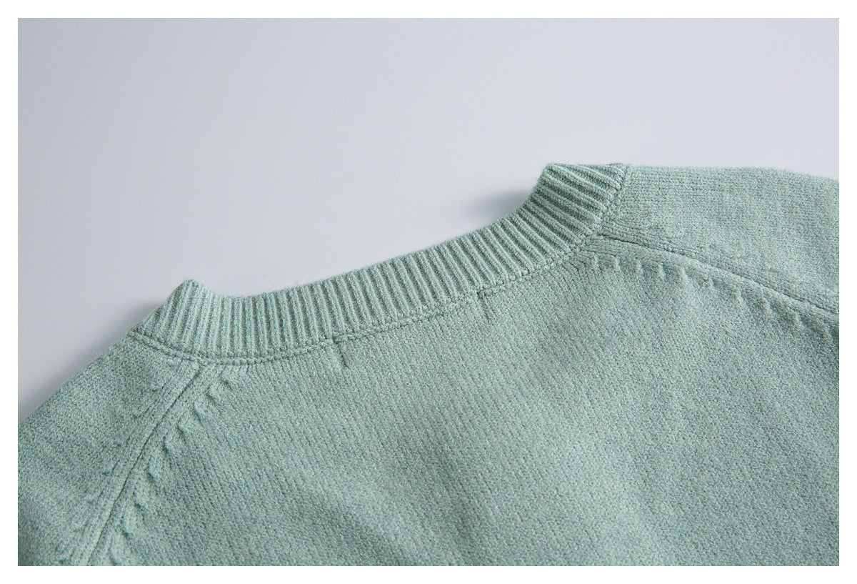 Close-up of the pale sage-green sweater's ribbed crew neckline and shoulder seams.