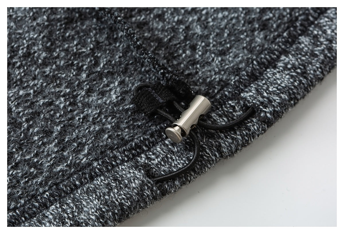 Close-up of a black drawcord and silver toggle at the edge of charcoal marled knit fabric.