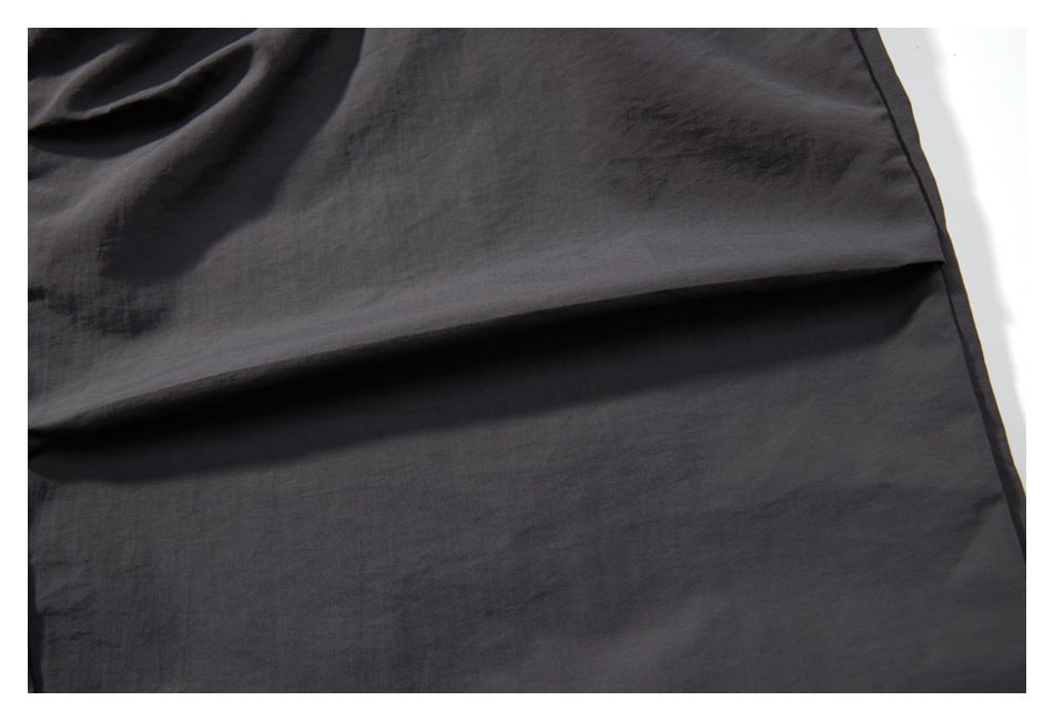 Close-up of dark charcoal garment fabric folded to show its smooth surface and stitched edge.