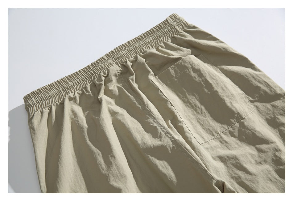 Beige trousers shown close up, with a gathered elastic waistband and a large front patch pocket.