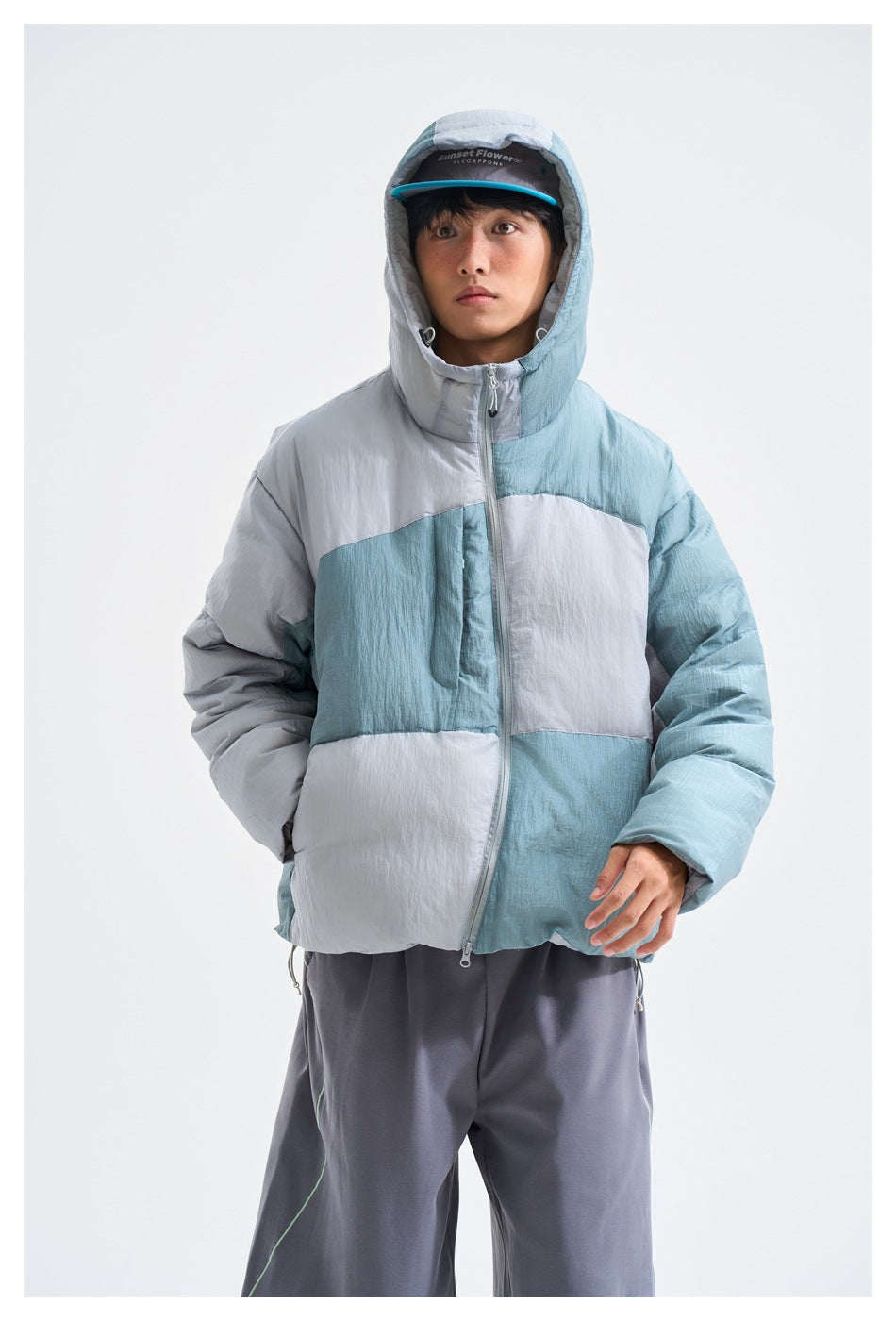 Front view of a model wearing a blue-gray color-block hooded puffer jacket with a front zip.