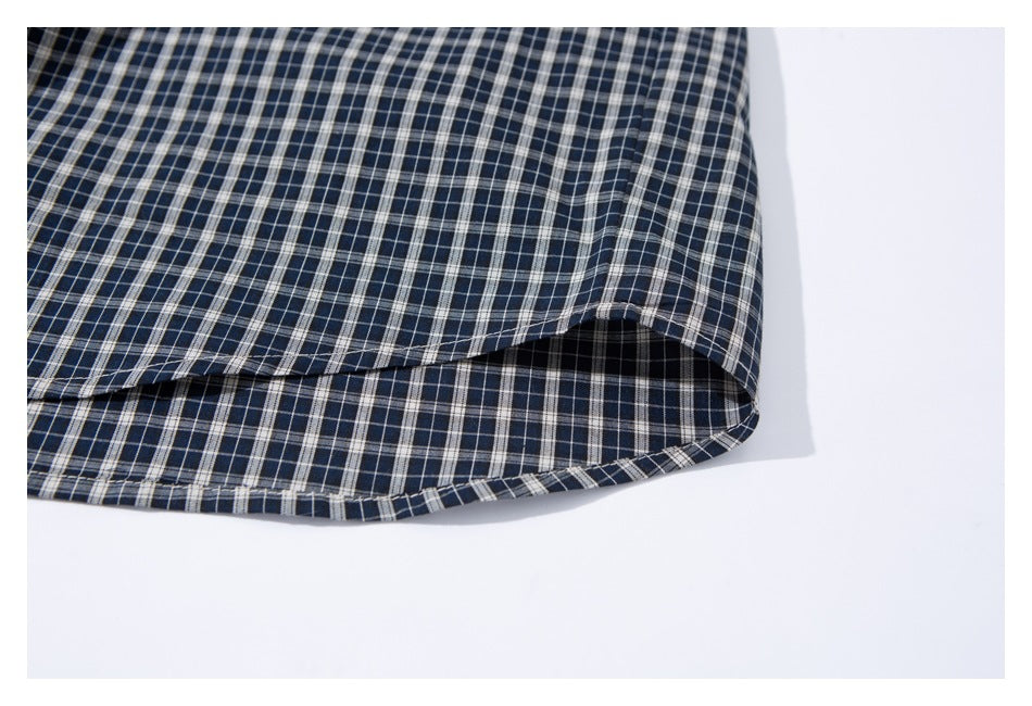 Close-up of the curved hem and stitching on a navy checked shirt.