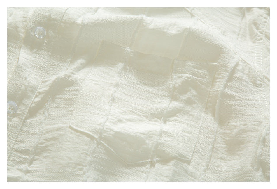 Close-up of an ivory shirt front with buttons, a patch pocket, and alternating woven-texture panels.