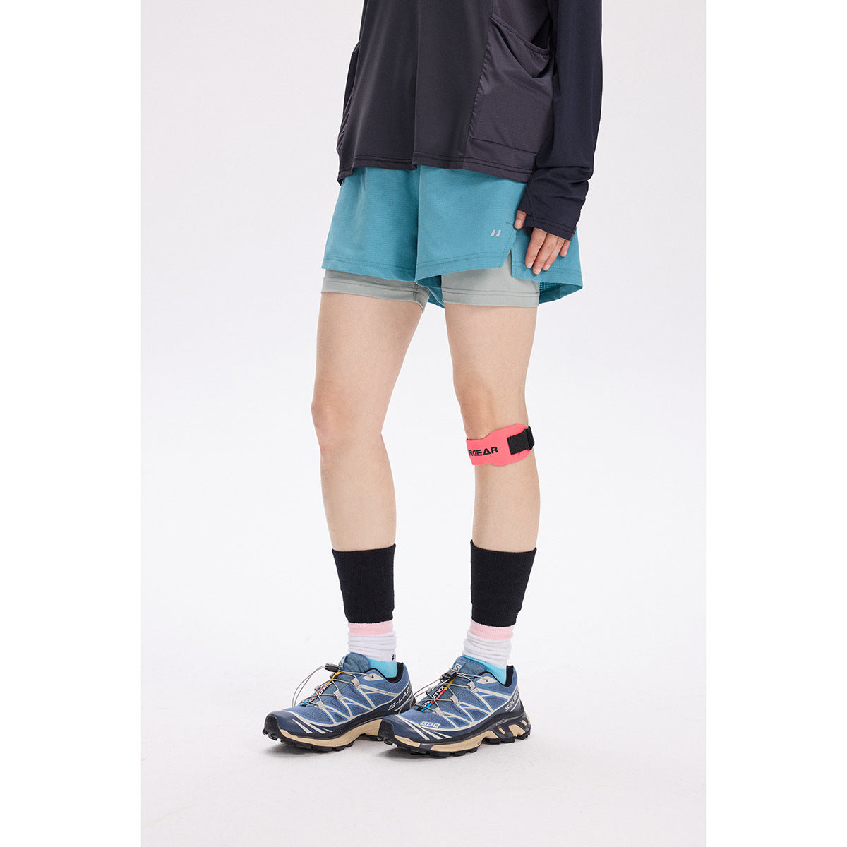 Cropped view of a model wearing turquoise running shorts over gray liner shorts, with a dark top.