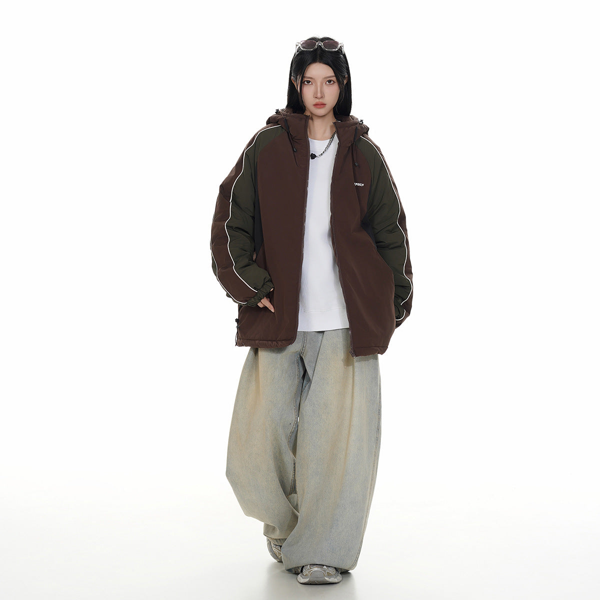 Model wearing a brown hooded jacket with olive sleeves and white piping, paired with loose light-wash jeans.