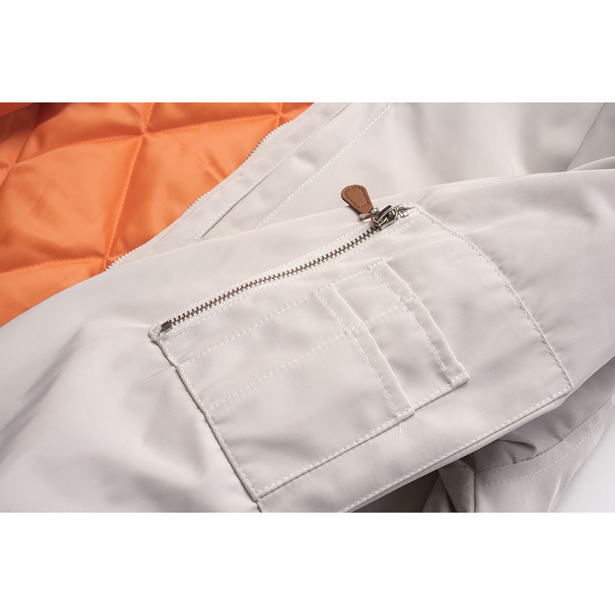 Close-up of a pale gray jacket sleeve with a zip pocket, showing orange quilted lining behind it.