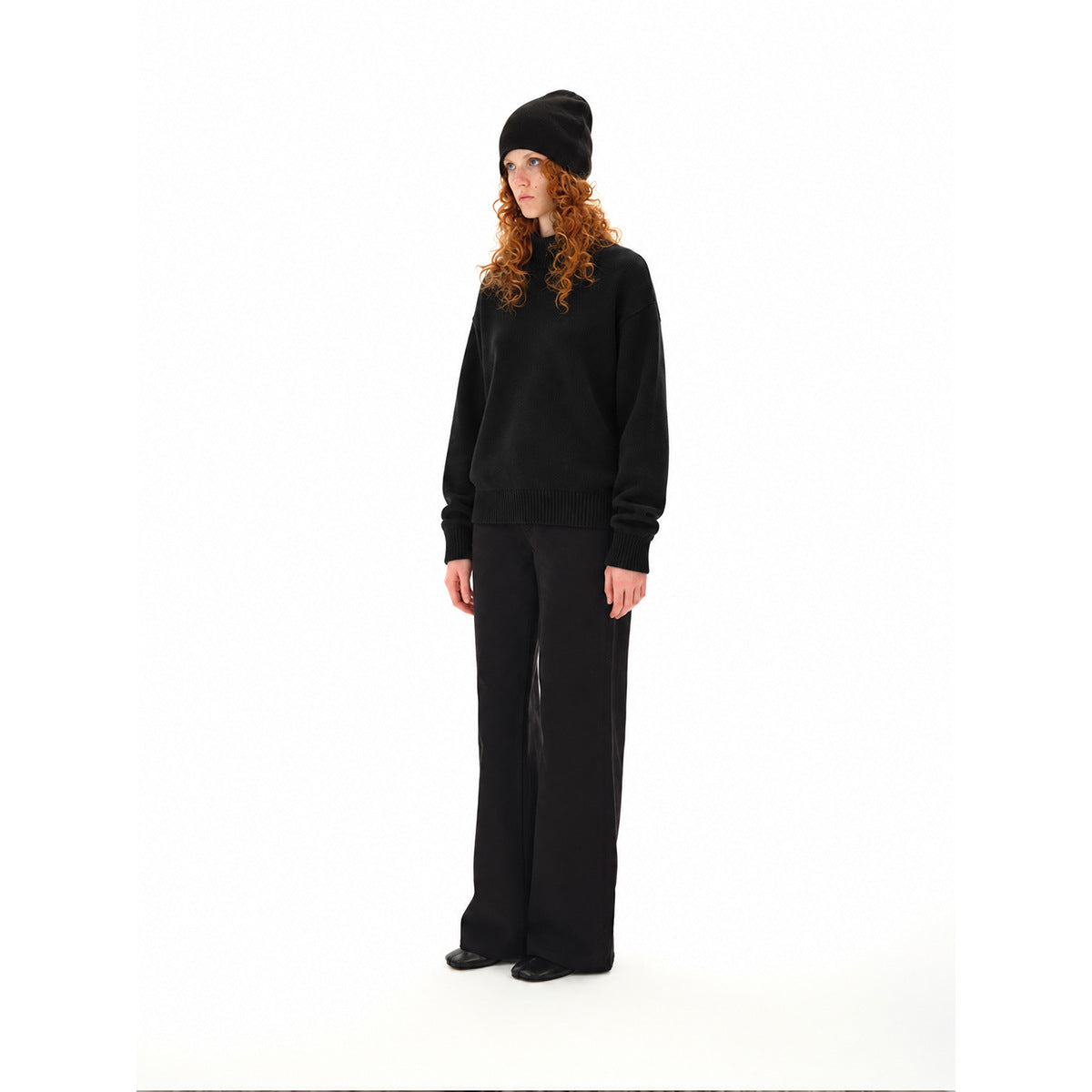 Model wearing a black rib-trimmed sweater, black beanie, and wide-leg trousers.
