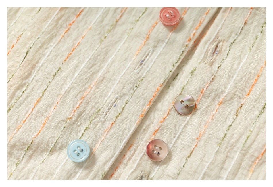 Detailed view of colorful buttons and buttonholes on an ivory shirt with raised orange and olive stripes.