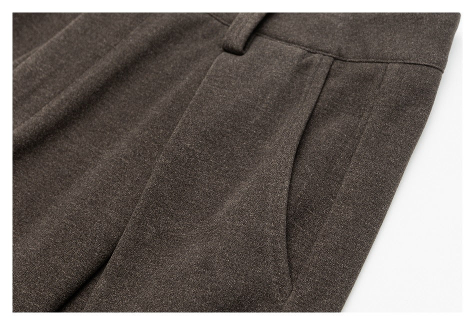 Close-up of dark brown trousers showing a seam and curved pocket opening.
