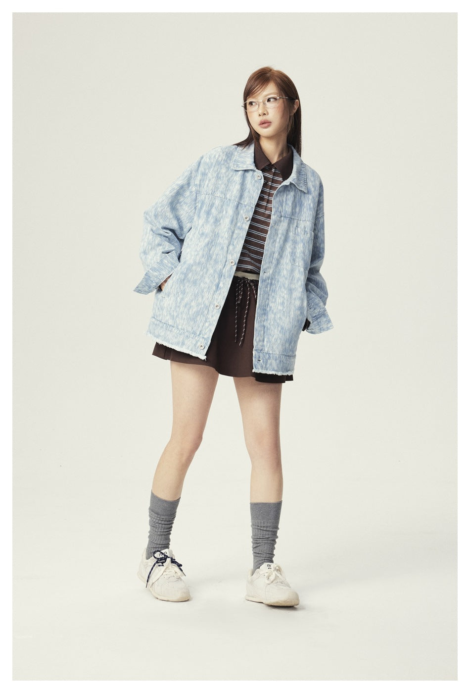 Model wearing an oversized light blue patterned jacket over a brown striped polo and dark shorts.