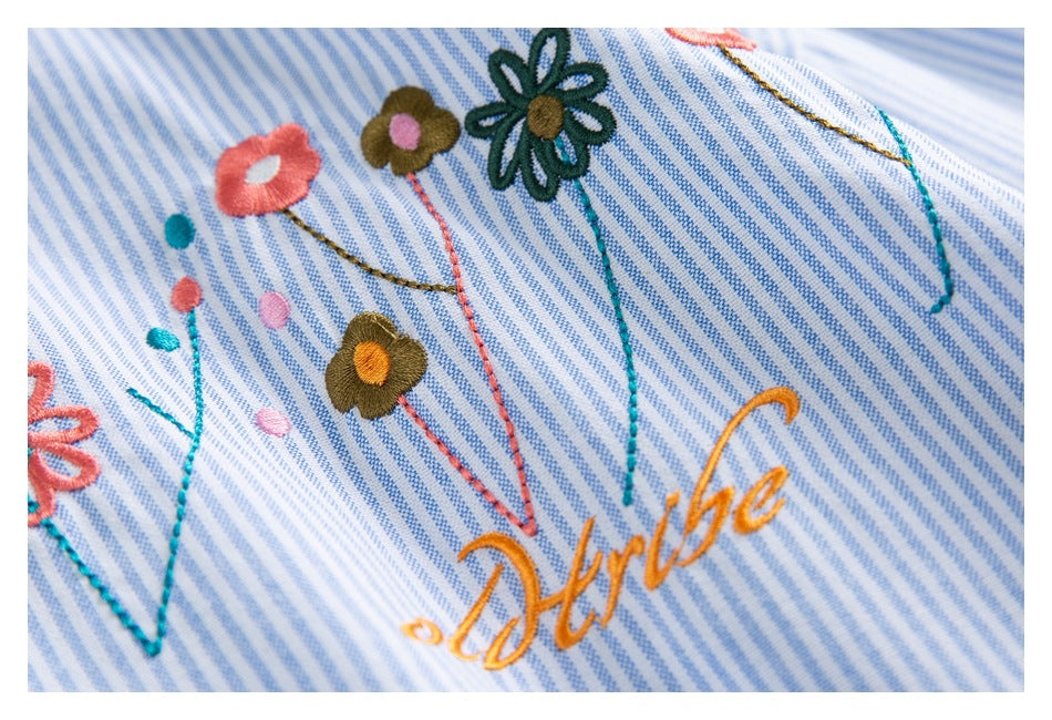Close-up of colorful embroidered flowers and cursive lettering on blue-and-white striped fabric.