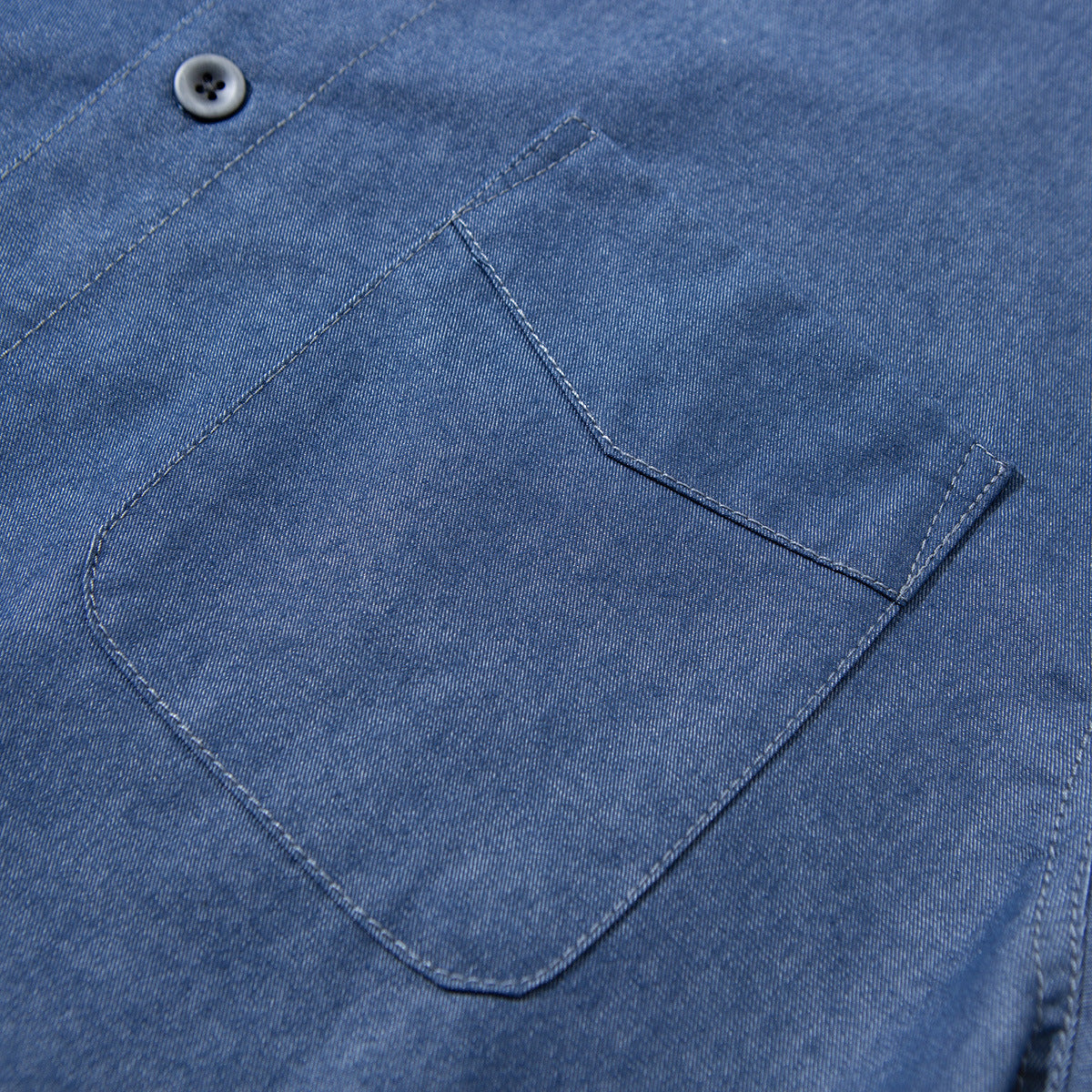Close-up of the blue shirt's single chest pocket, curved lower corners and buttoned flap.