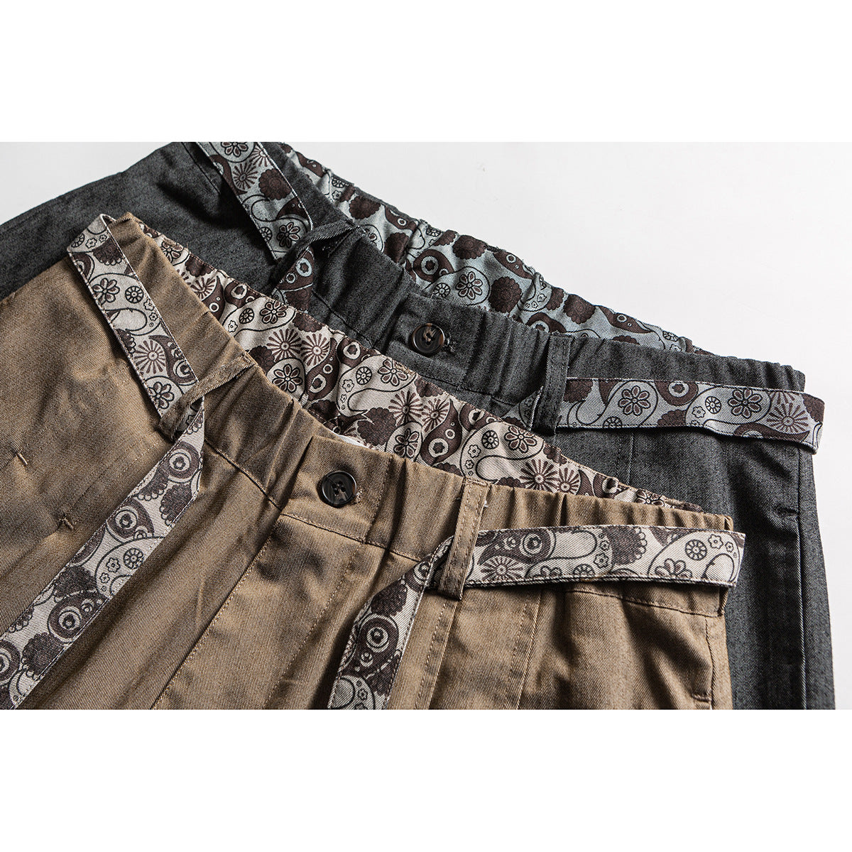 Close-up of charcoal and tan trousers showing patterned waistband lining, belt loops, buttons and matching printed straps.