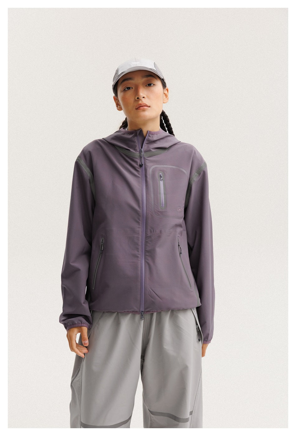 Closer front view of a model in a muted purple hooded jacket with zip pockets and gray pants.
