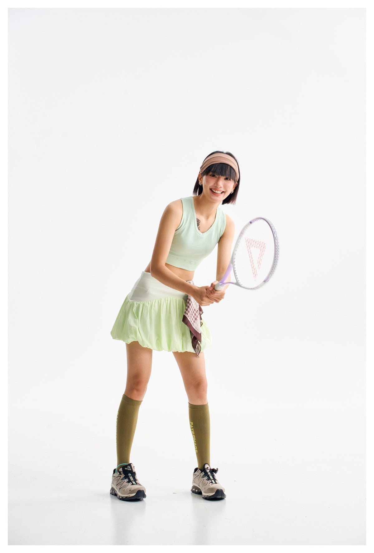 Model wearing a pale lime-green bubble skirt and mint crop top, holding a tennis racket.