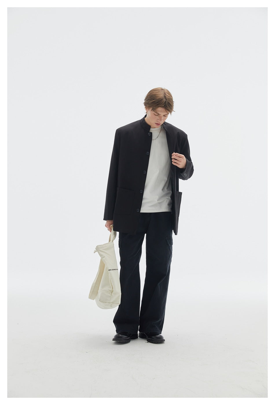 Full-length model wearing a black button-front jacket with a stand collar, white T-shirt and loose black cargo trousers.