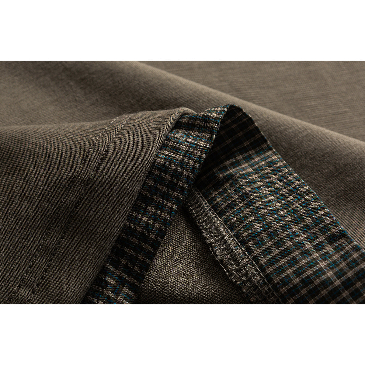 Close-up of a taupe sleeve hem and exposed overlocked edge beside brown and teal plaid fabric.