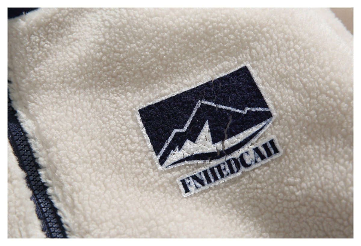 Close-up of an embroidered mountain logo on cream sherpa fabric beside a dark zipper.