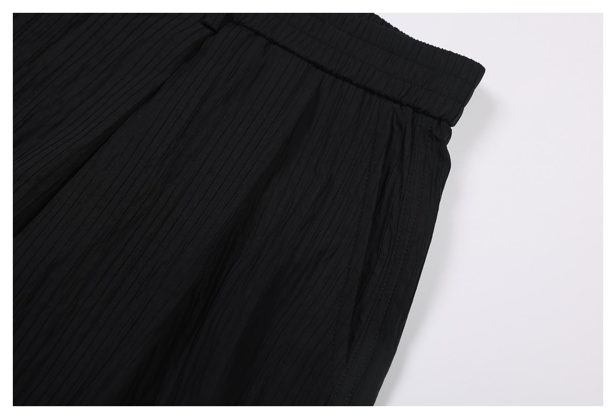 Close-up of black trousers showing a side seam, waistband, and narrow vertical pleats.