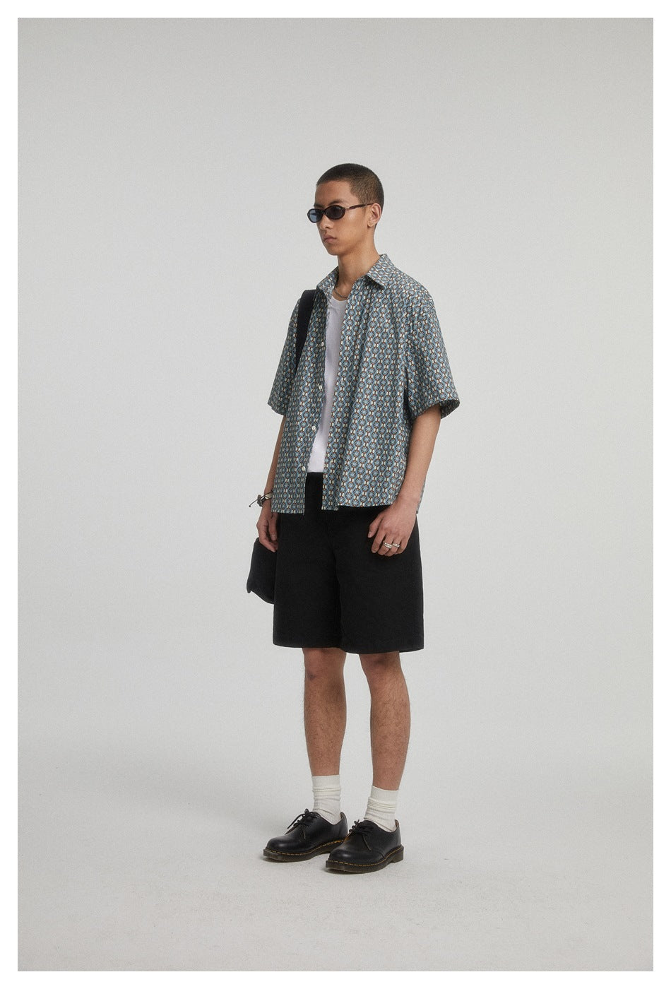 Three-quarter view of a model wearing a blue geometric-pattern short-sleeve shirt over a white tee.