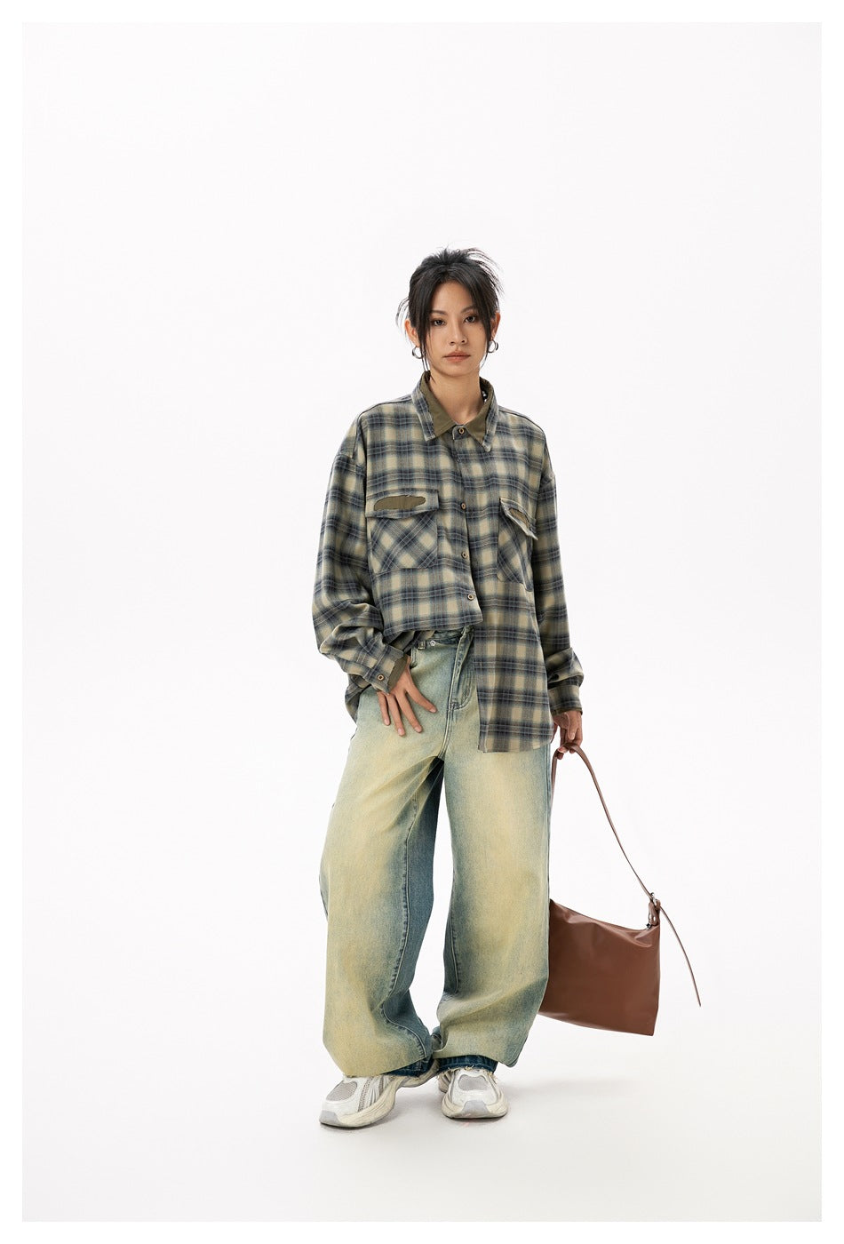 Full-length model wearing an oversized olive, beige and dark plaid shirt with wide faded jeans.
