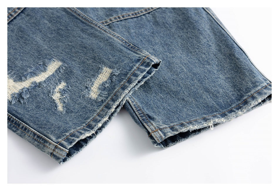 Close-up of distressed blue jean leg hems with fraying and light-colored torn patches.