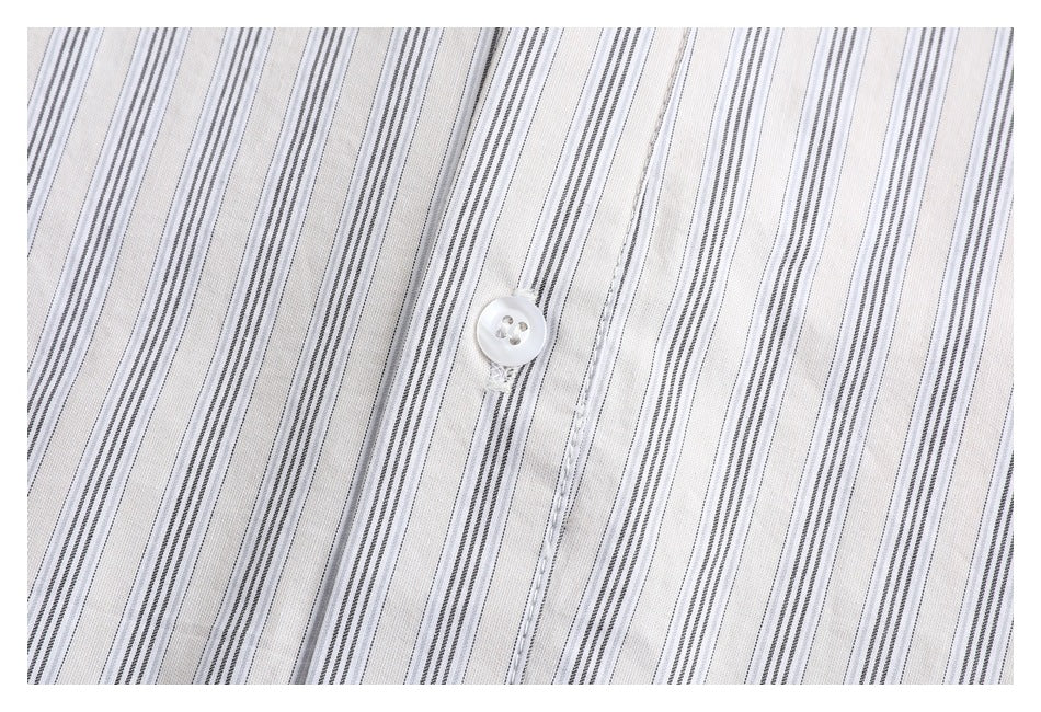 Close-up of a white button and placket on white fabric with fine gray vertical stripes.