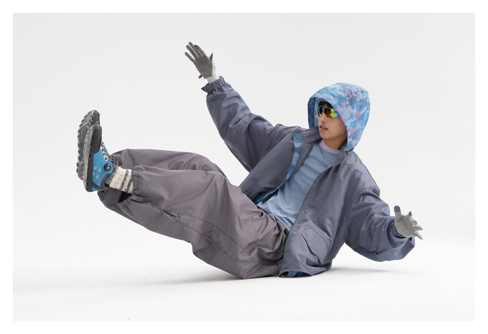 A man wears a slate-gray oversized jacket and loose pants, with a blue patterned hood, shown in a playful seated pose.