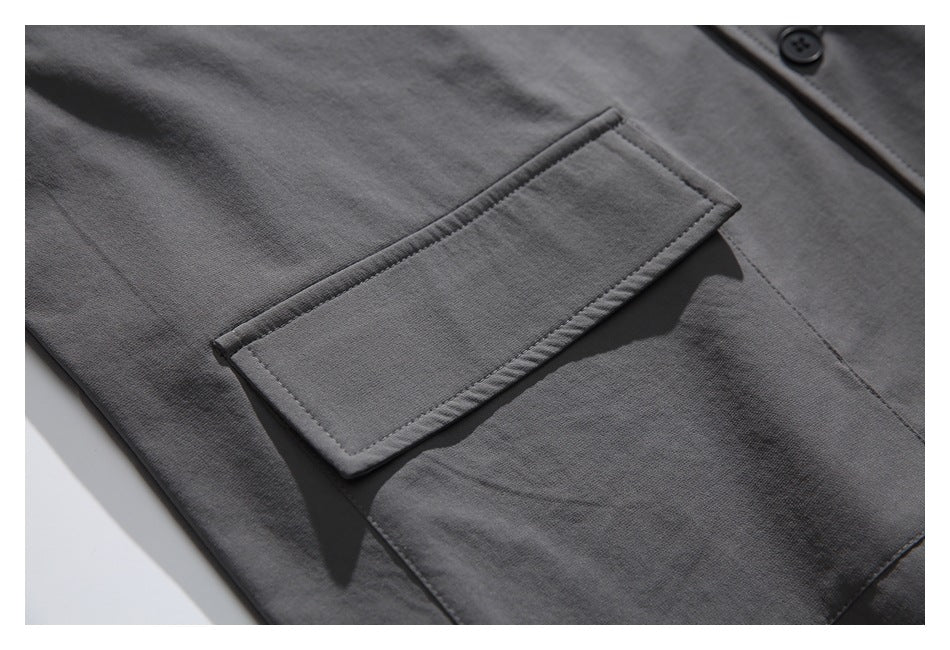 Close-up of a charcoal gray jacket pocket with a wide rectangular flap and visible stitching.