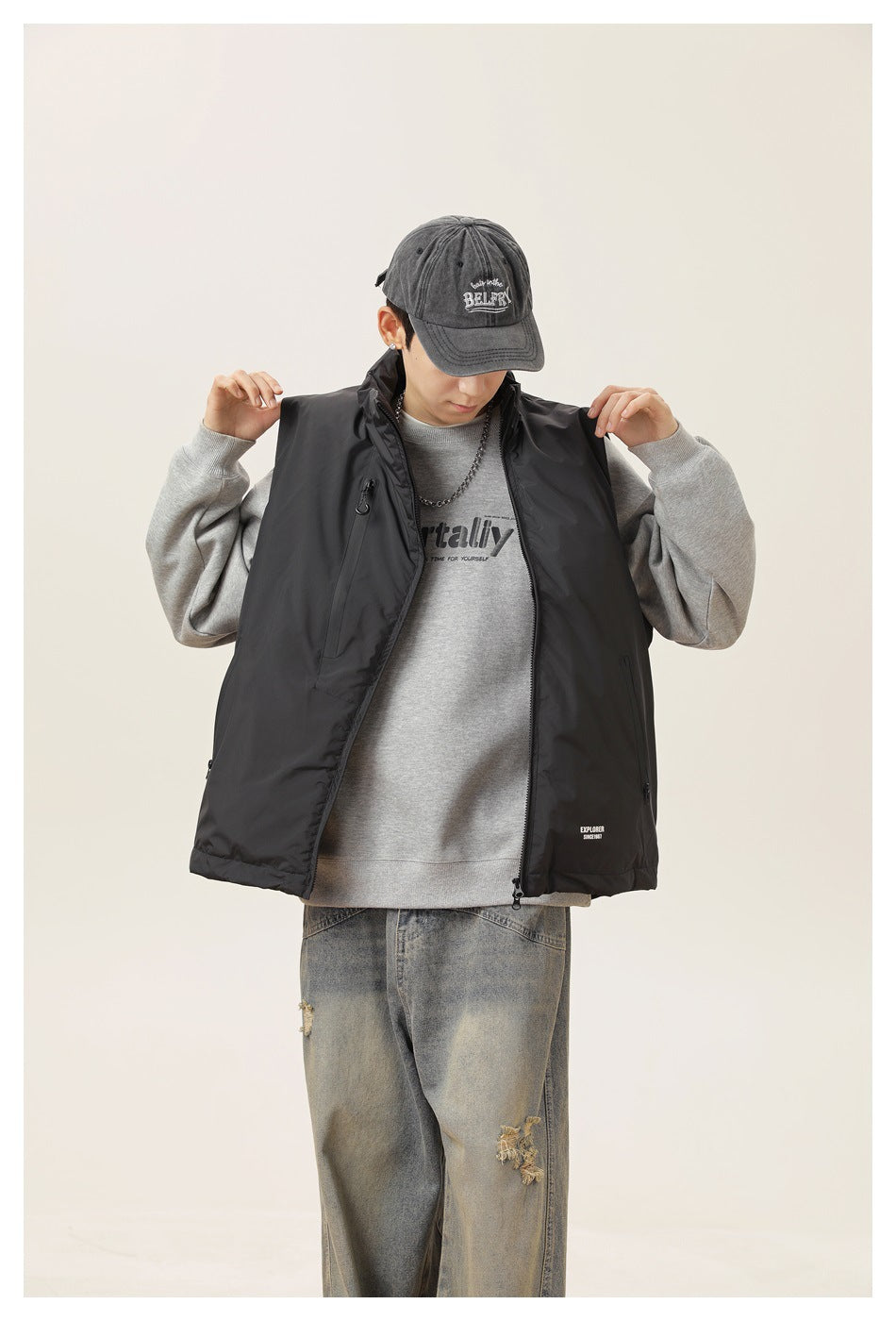 Close view of a model wearing a black zip vest over a gray graphic sweatshirt, adjusting the shoulders