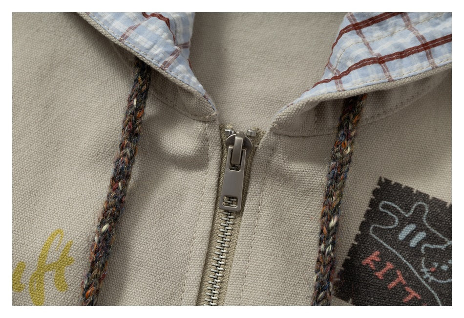 Close-up of a beige zip-front hoodie with multicolored drawstrings, plaid hood lining and cropped printed graphics.
