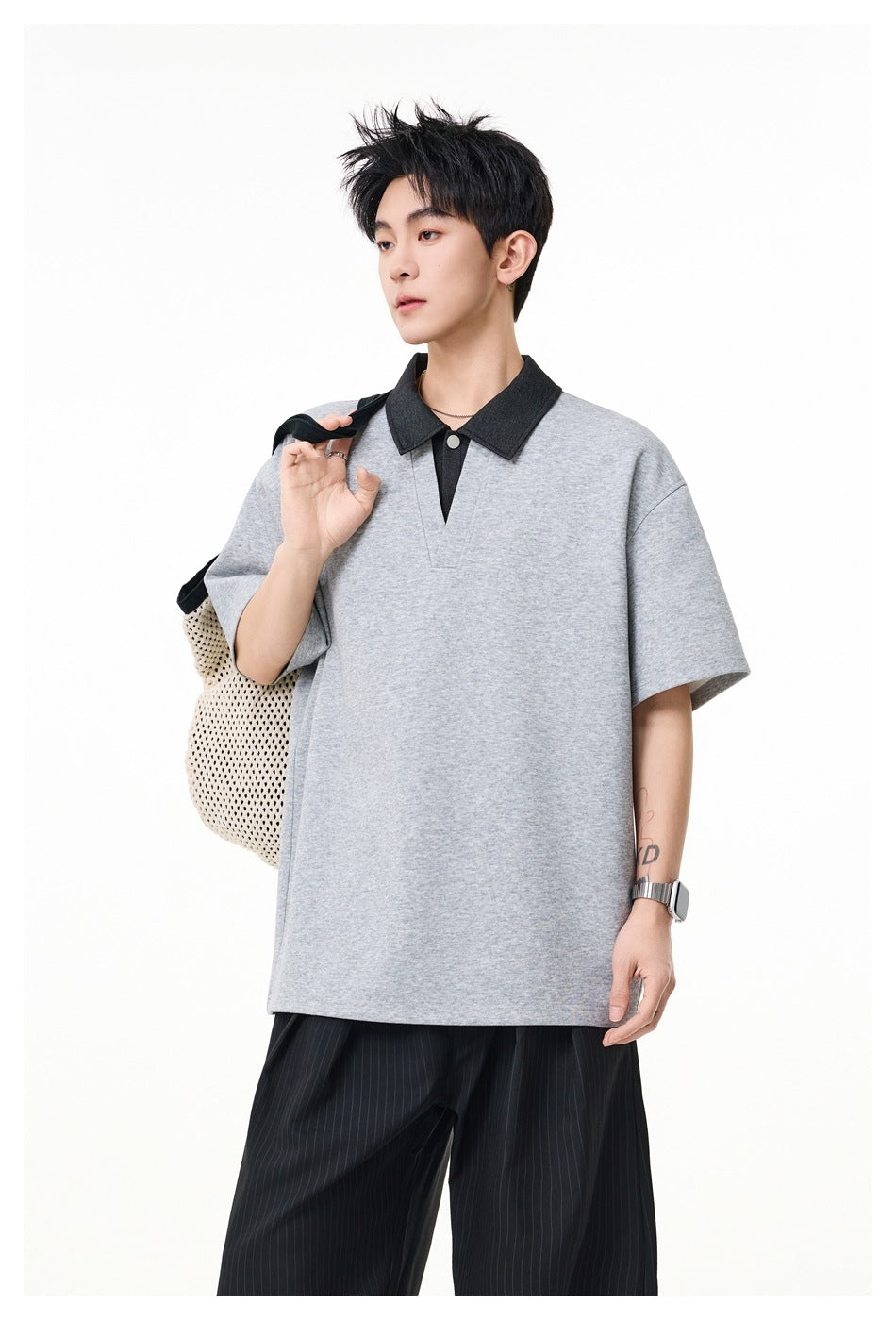 Model wearing a gray short-sleeve polo with a dark collar and black pinstripe trousers, carrying a mesh bag.