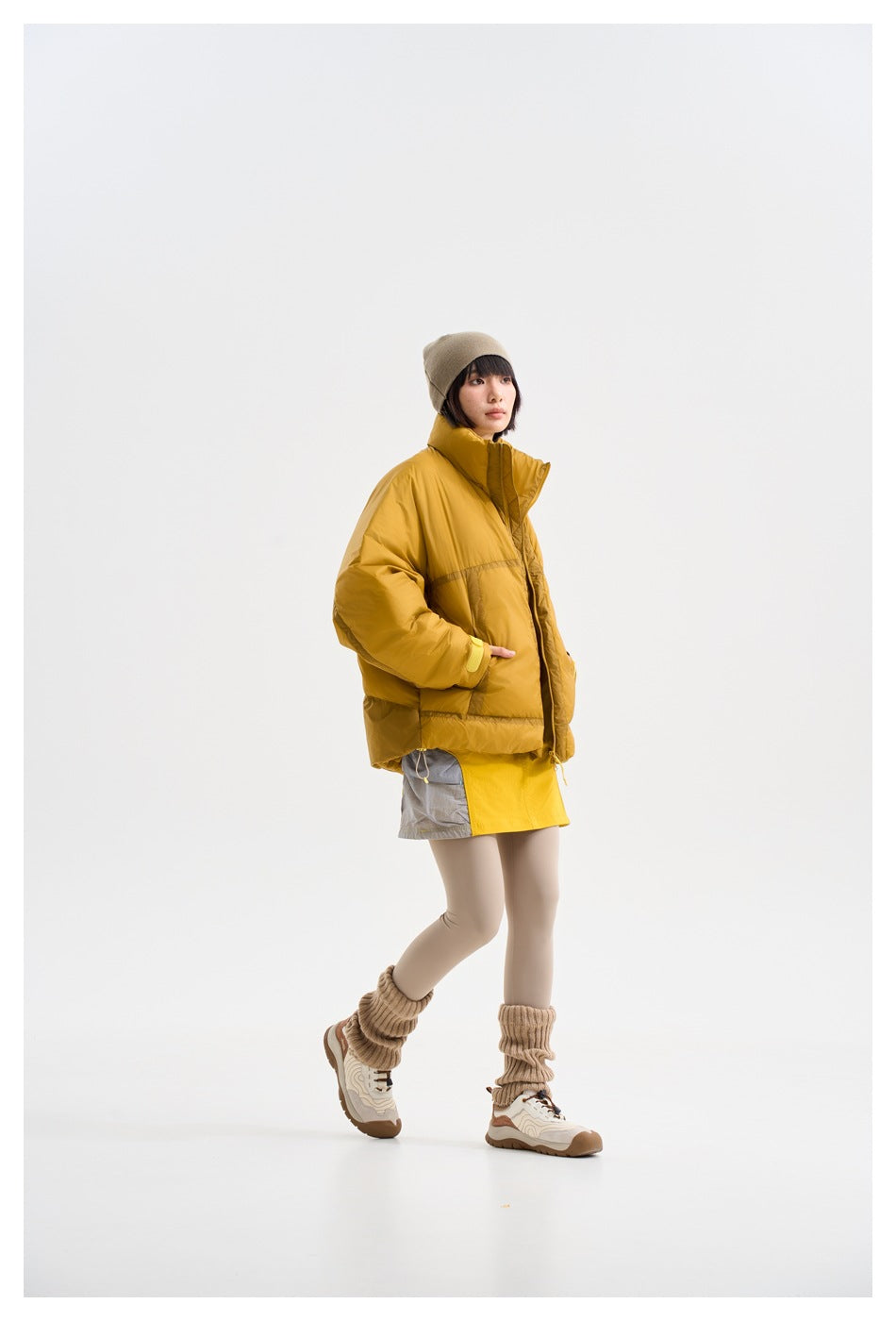 Model walking in a mustard-yellow padded jacket, shown from a three-quarter side view.
