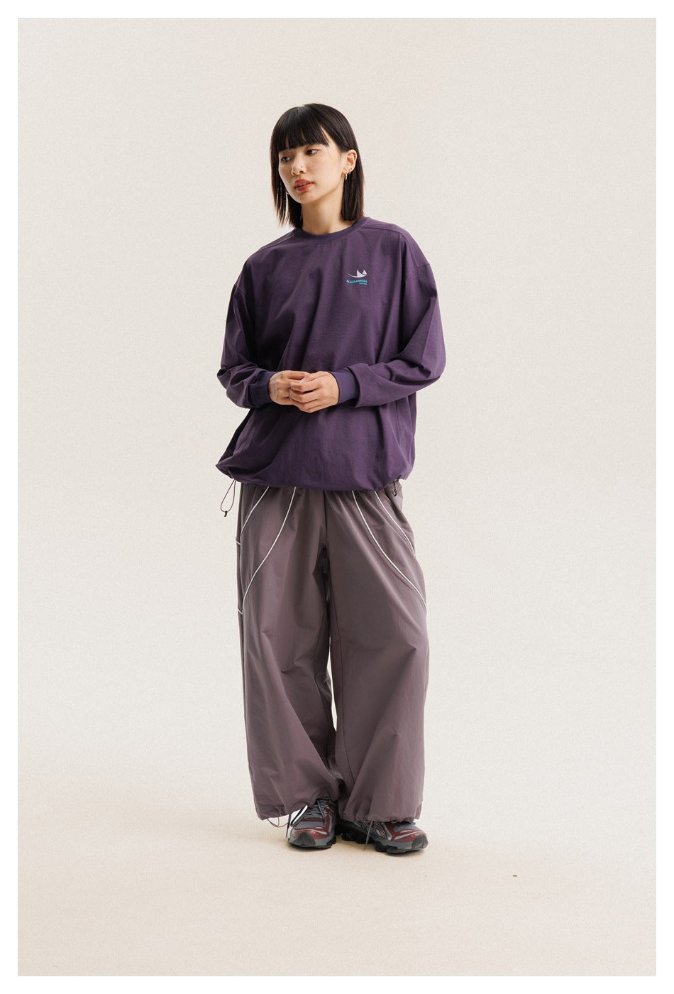 Front view of a model in an oversized purple long-sleeve shirt and loose gray-mauve pants.