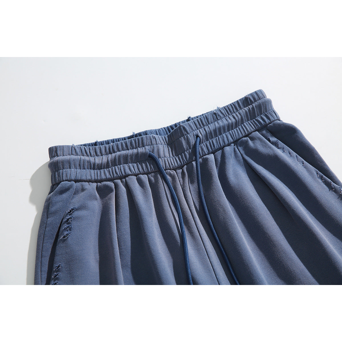 Close-up of slate-blue pants with a gathered elastic waistband, drawstrings, and distressed stitching.