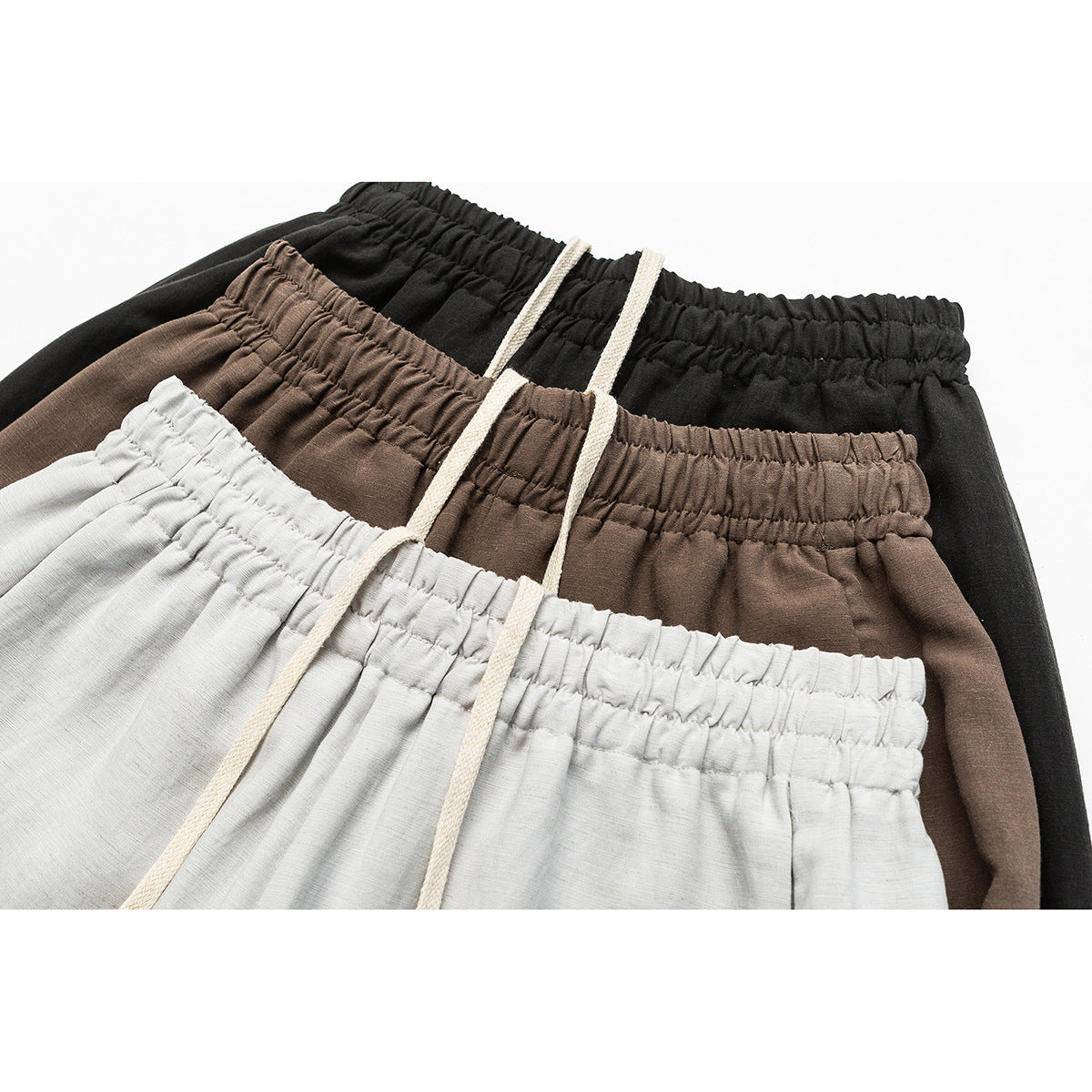 Close-up of elastic-waist trousers in light gray, brown, and black with cream drawstrings.