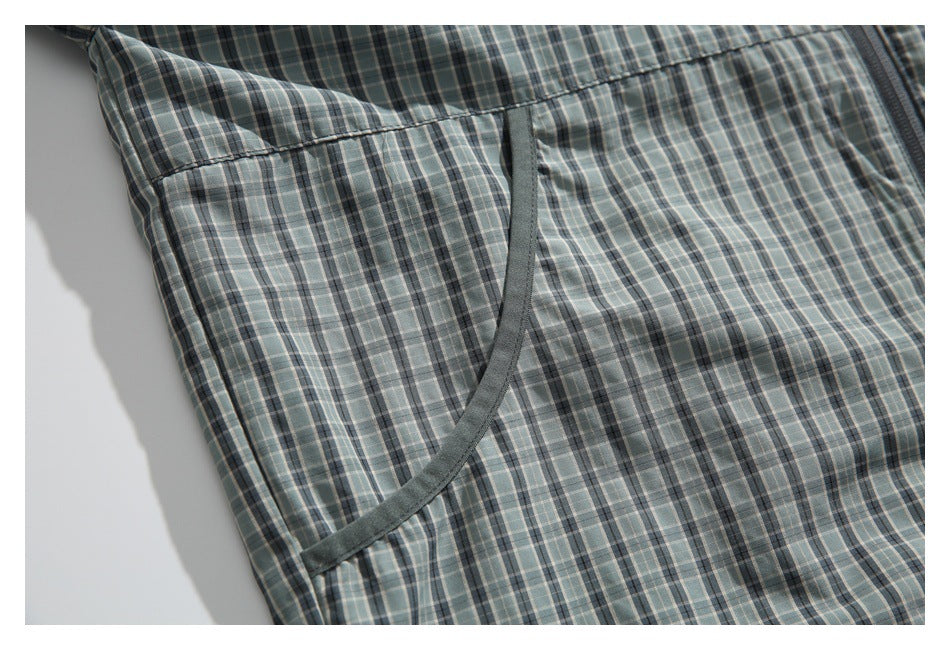 Close-up of a curved, dark-trimmed pocket on a gray-green plaid jacket.