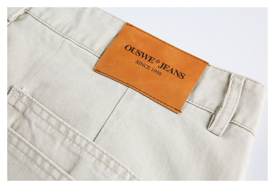 Close-up of light beige jeans showing the waistband, belt loop, stitching, and brown OUSWE Jeans label.