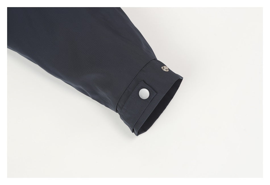 Close-up of a dark jacket sleeve ending in a cuff with a silver snap fastener.