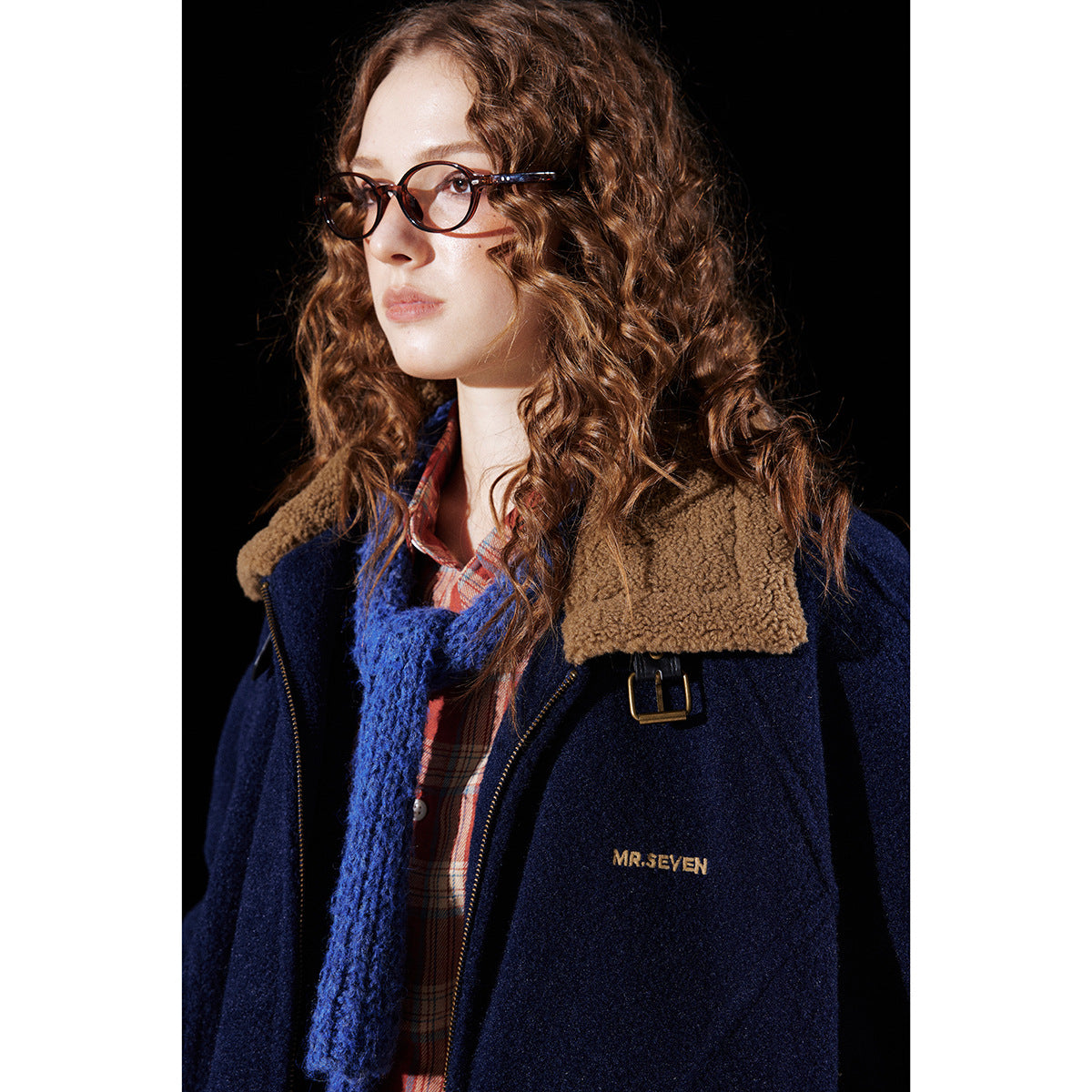Close-up of a model in a navy jacket with a tan sherpa collar and brass-colored buckle detail.