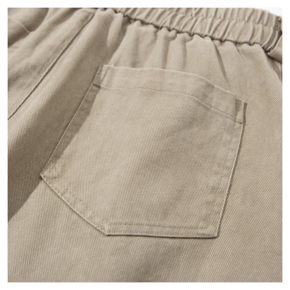 Close-up of a beige garment's elastic waistband and stitched back patch pocket.