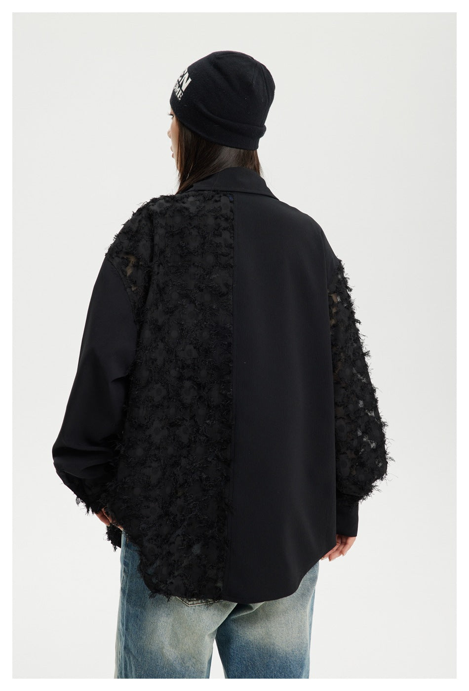 Rear view of a model wearing a black shirt with a large smooth back panel and textured side and sleeve panels.