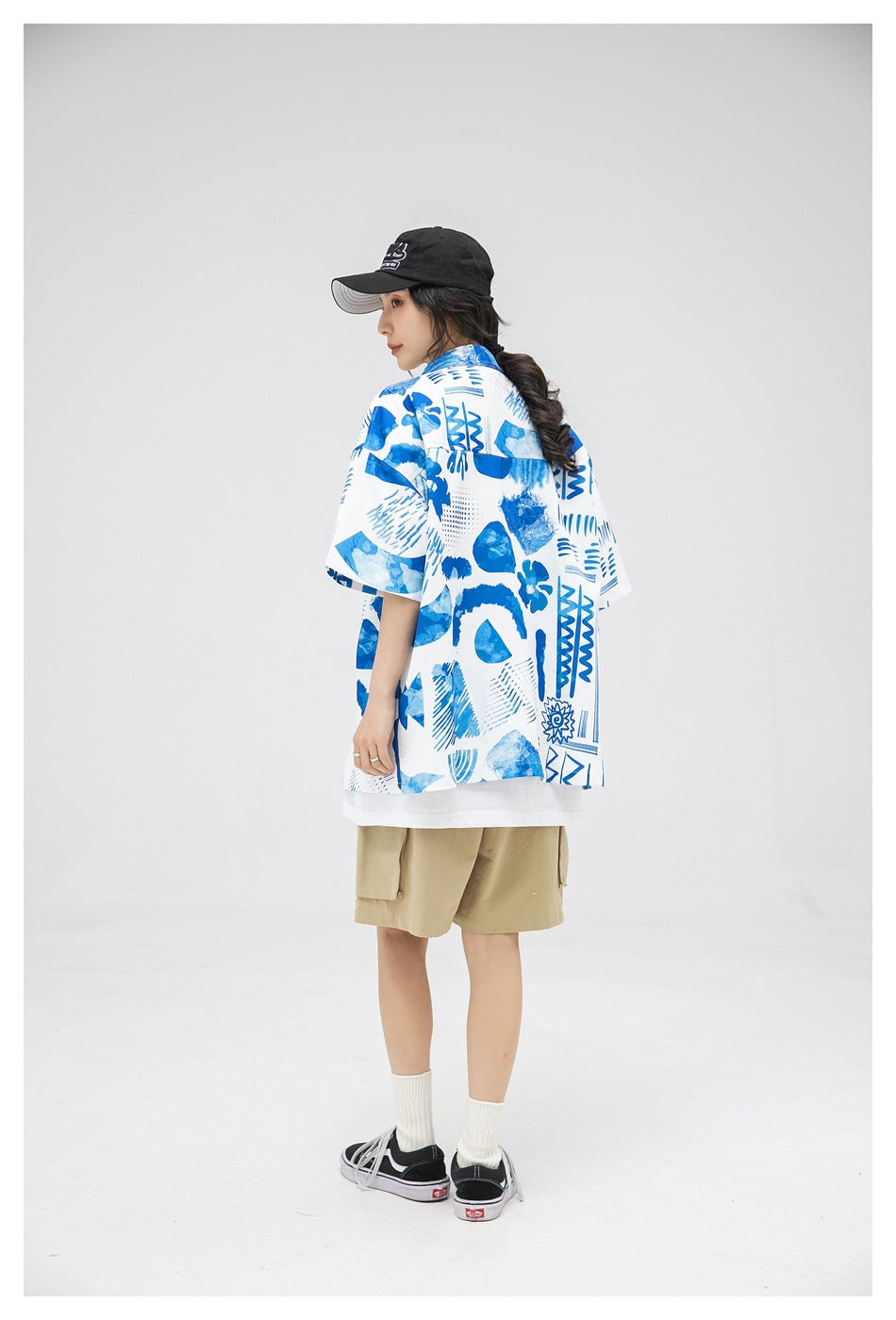 Model in a white and blue abstract-print short-sleeve shirt, shown from the back at an angle with khaki shorts.