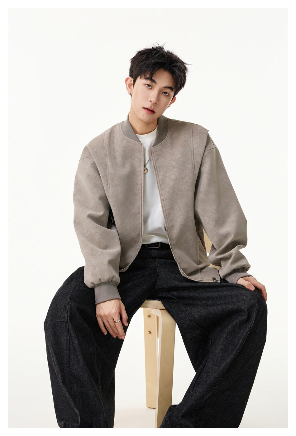 Seated model wearing an open light taupe zip-front jacket with ribbed collar and cuffs.