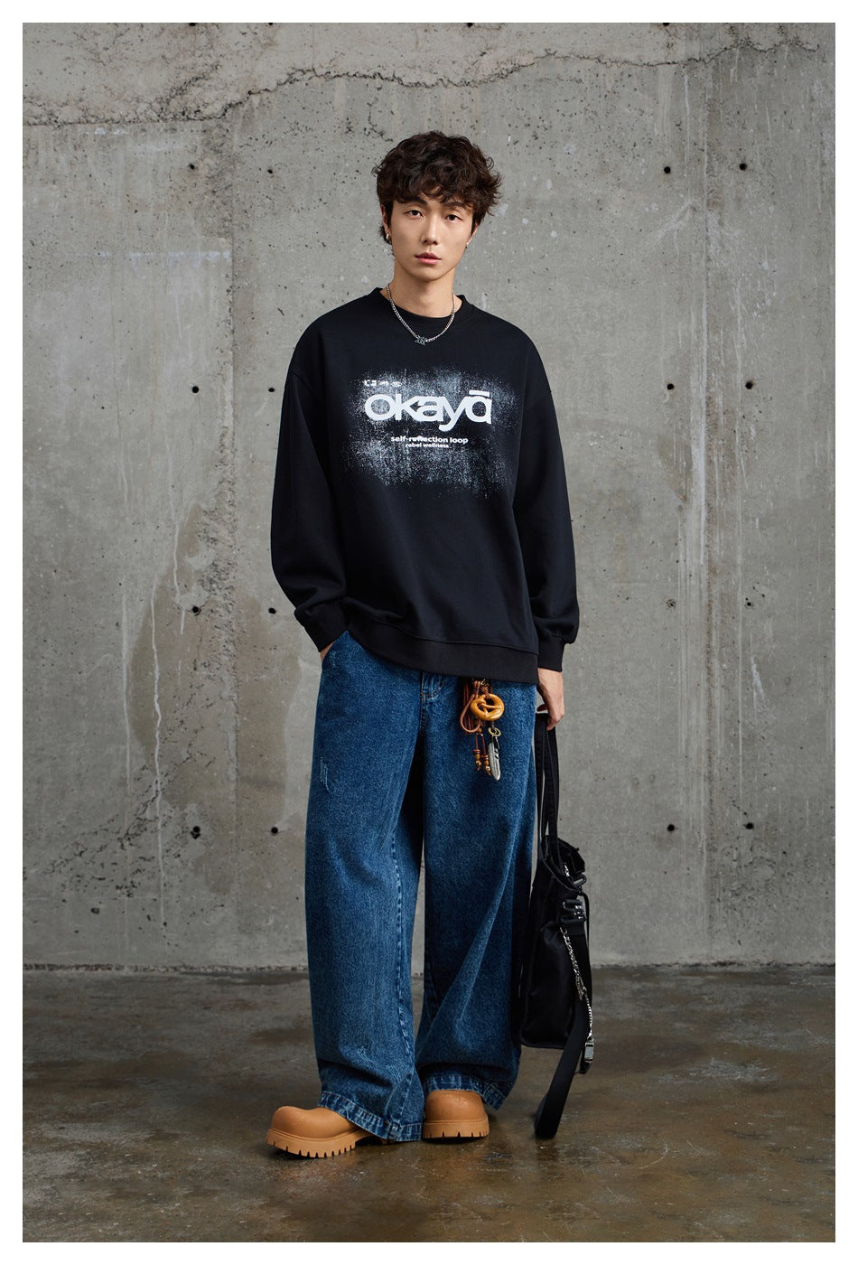 Full-length model wearing a black graphic sweatshirt with loose blue jeans and tan boots.