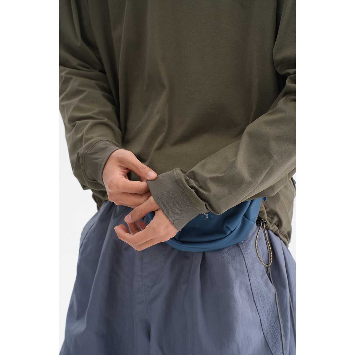 Close-up of an olive shirt's ribbed cuff and hem area above slate-blue pants.