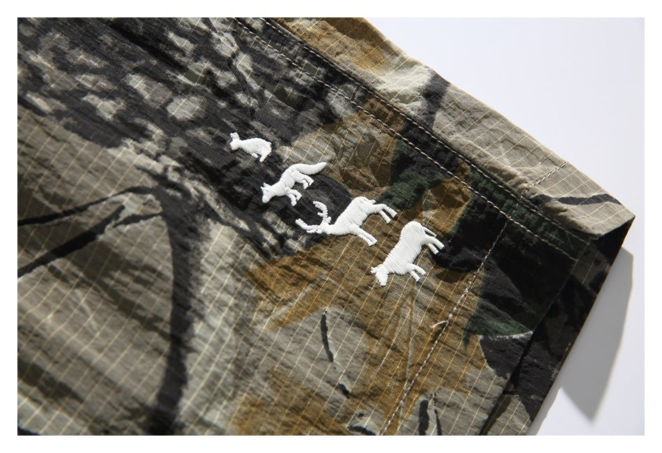 Close-up of small white embroidered animal silhouettes on the camouflage shorts.