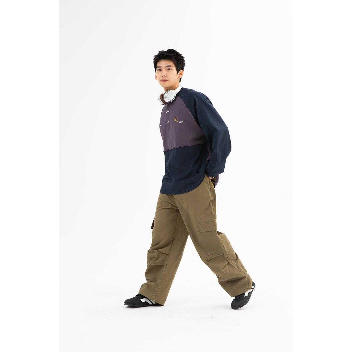 Model wearing a navy and muted purple color-block raglan sweatshirt with small chest graphics and olive cargo pants.