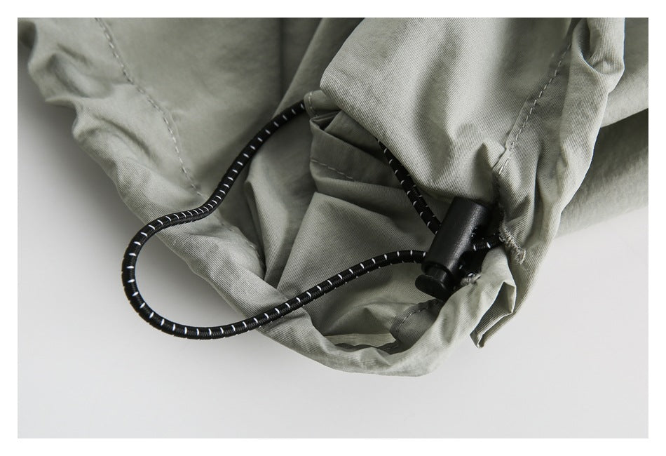 Close-up of an olive-gray garment hem with a black elastic drawcord and toggle.
