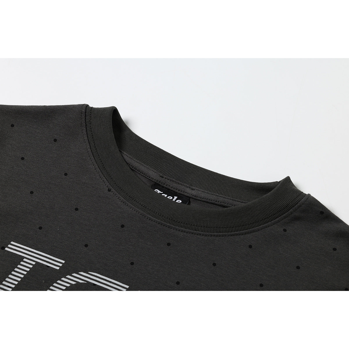 Close-up of a charcoal crew-neck T-shirt with small black dots, ribbed collar stitching, and part of a white chest print.